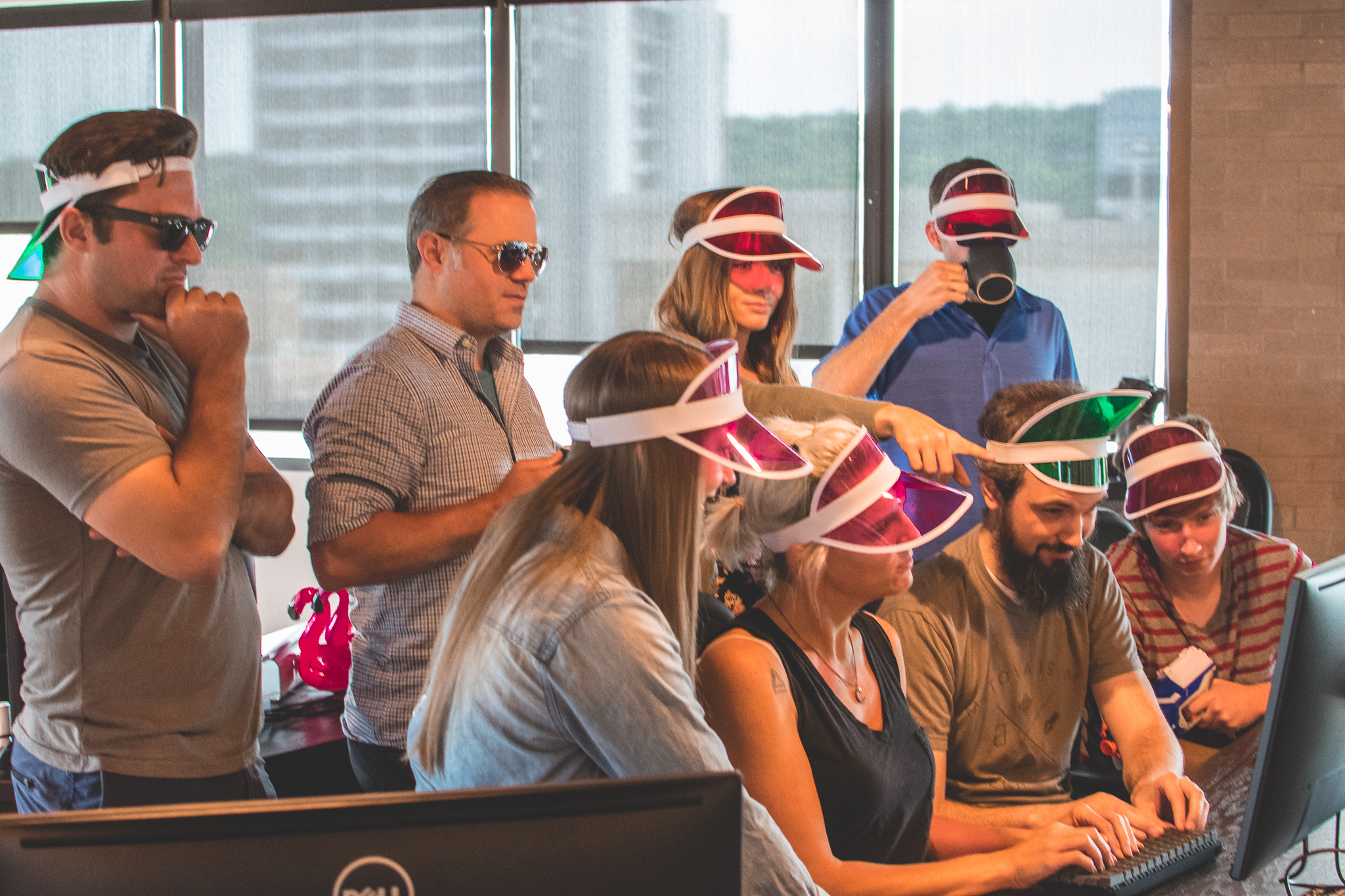 LorenzoGarnett_Fayetteville_office funny1 – Lorenzo Garnett Eight coworkers wearing bright sun visors, collaborating at one computer - Metova Fayetteville Office